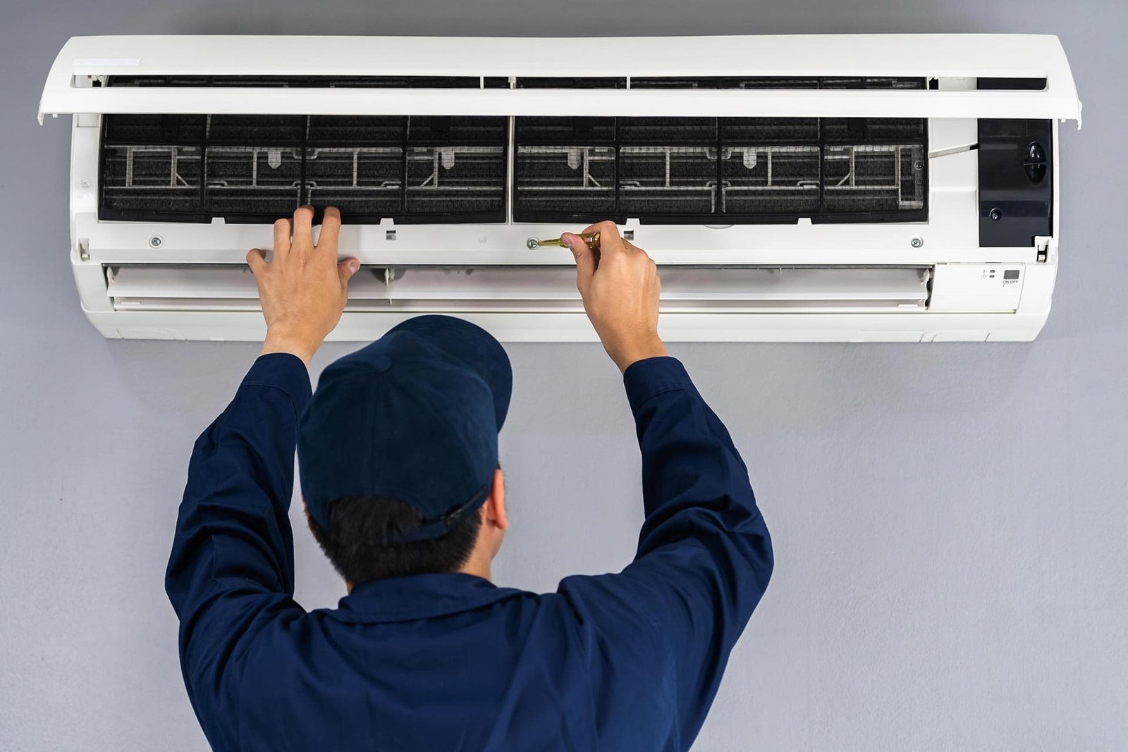 Technician servicing wall-mounted air conditioning unit for cooling system repair.